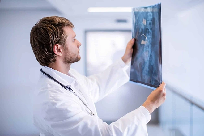 Doctor in white coat reviewing a patient's spine X-ray in a hospital hallway.