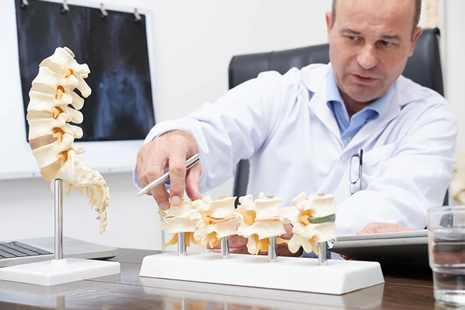 Doctor explaining effective disc decompression treatment using a spine model, with X-ray in background.