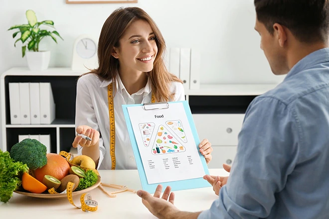 Holistic nutrition consultant discussing a healthy diet plan with a client, surrounded by fresh fruits and vegetables.