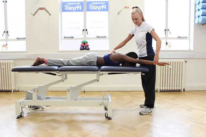 Physical therapist assisting a patient lying on a treatment table with arm exercises.