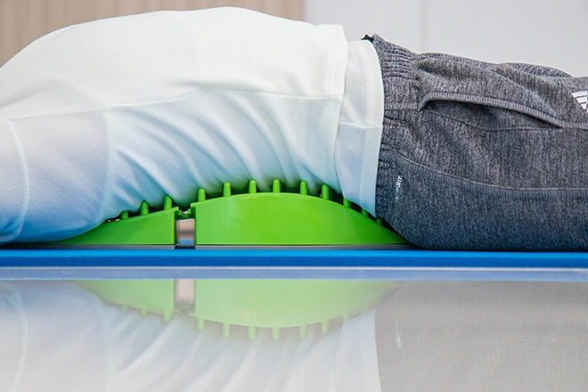 Person lying on a green decompression device to relieve back pain.