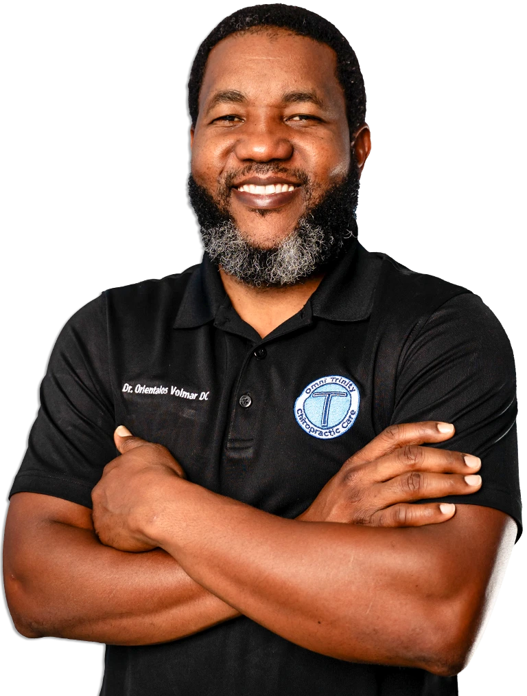 Dr. Orientalos Volmar, DC, a gentle chiropractor, smiles with arms crossed.