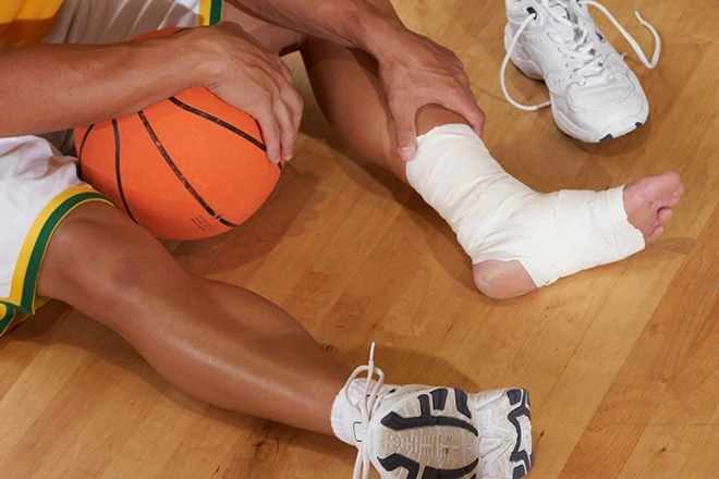Basketball player with a sprained ankle wrapped in bandage after injury on the court.