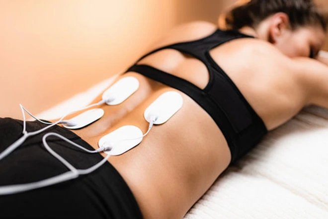 Woman receiving TENS therapy for back pain with electrodes on her lower back.